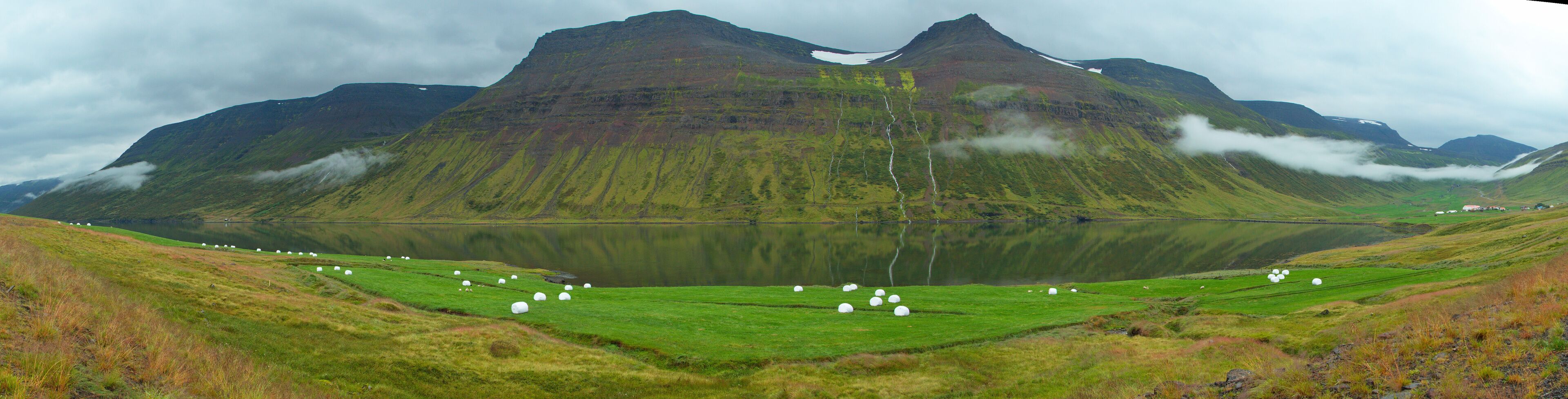 A mountainous landscape with a lake and grazing sheep.