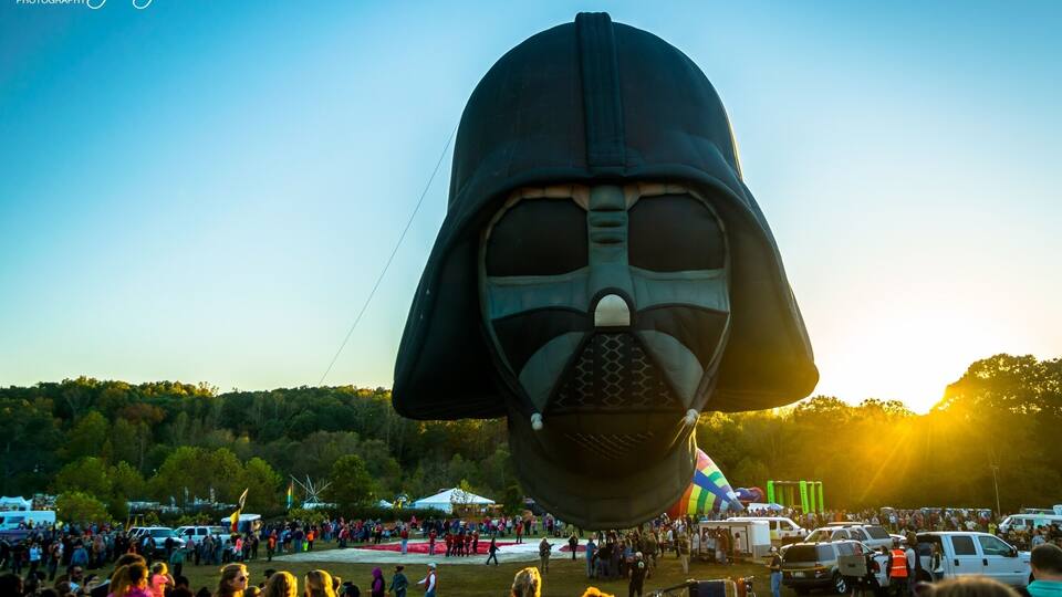 A large crowd at a festival with a prominent Darth Vader balloon.