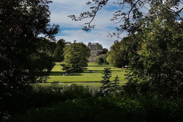 Un parc avec une grande pelouse, un étang et un bâtiment doté d’une tour, visible au loin.