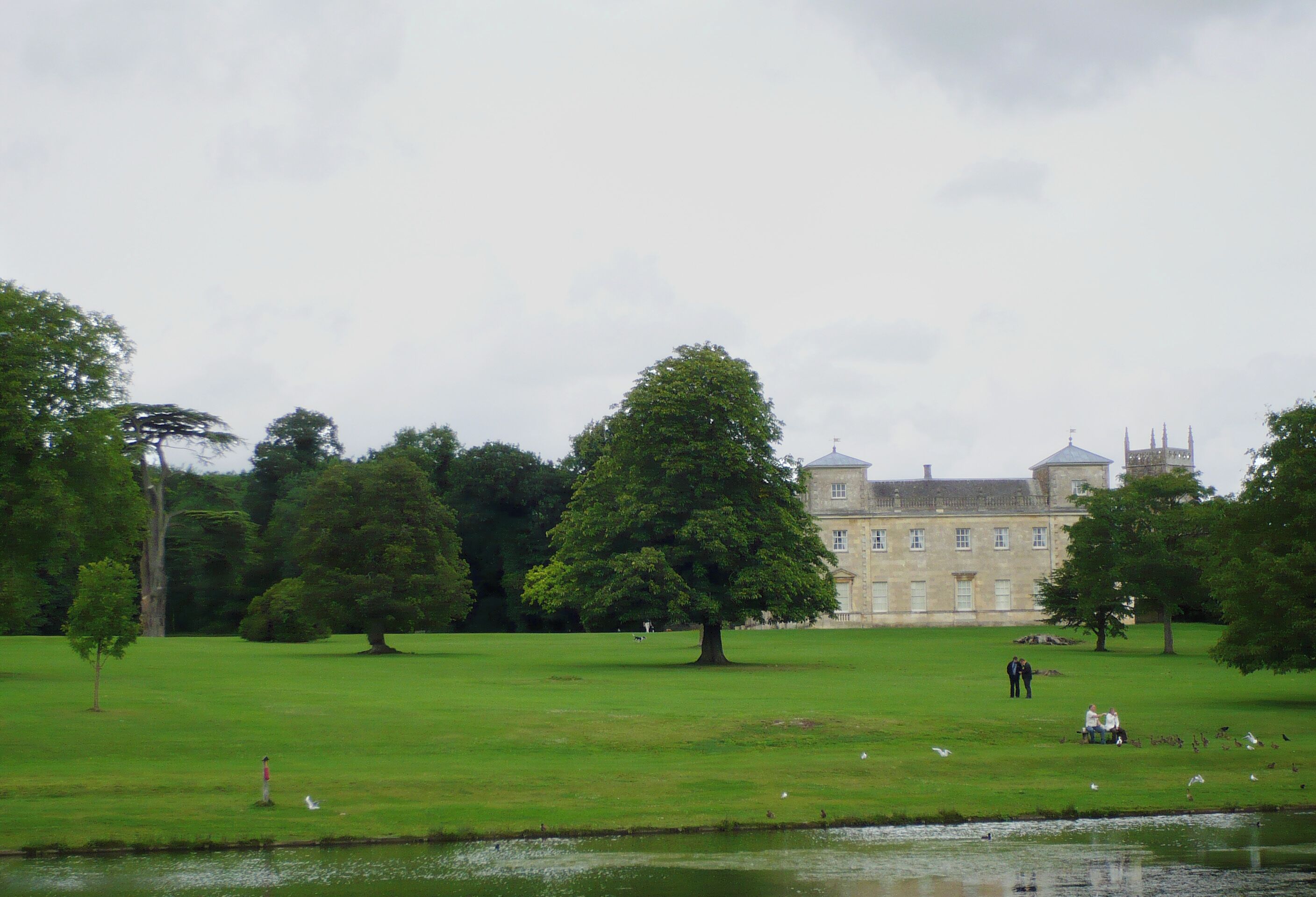 A large, historic building with a prominent tower, surrounded by lush green grass and trees.