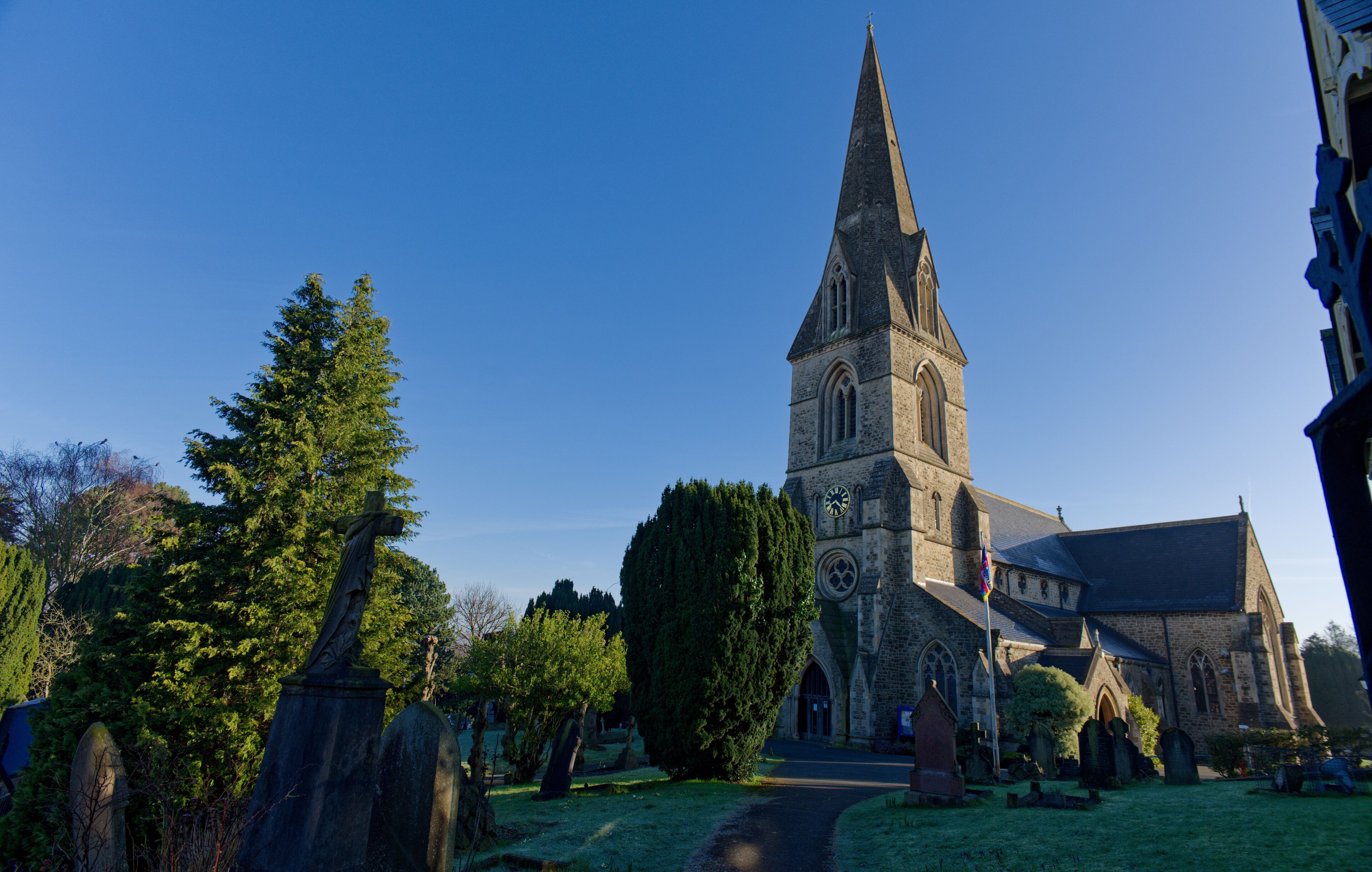Beautiful old Christ Church in Swindon, UK. Wide view of the church with graveyard and green trees. Footpath towards the entrance on a sunny morning with blue sky.