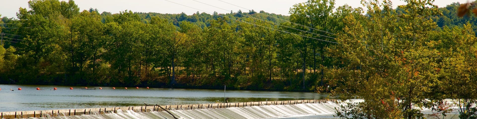 A dam with water flowing over it, surrounded by trees and a body of water.