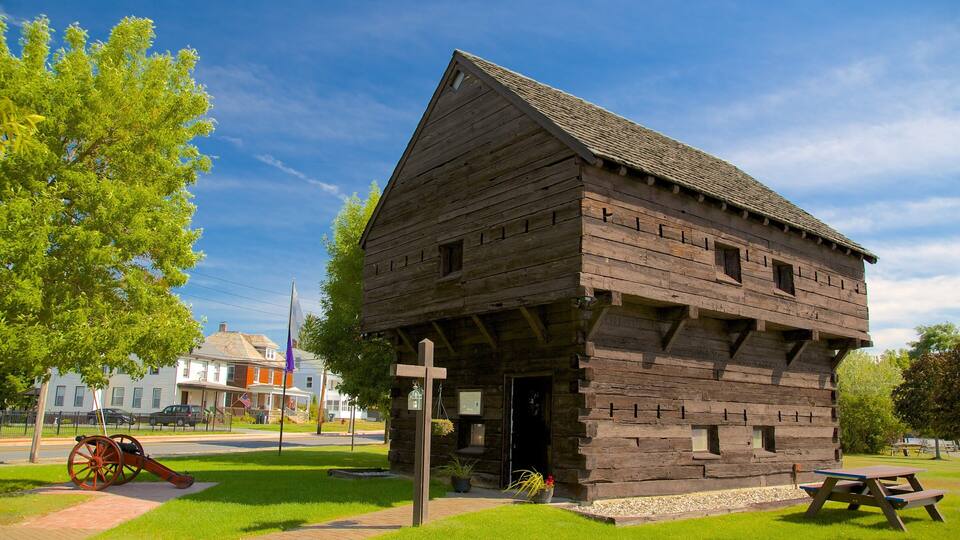 A wooden cabin with a steep roof, surrounded by grass and trees.