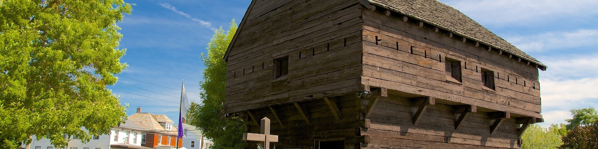 A wooden cabin with a steep roof, surrounded by grass and trees.