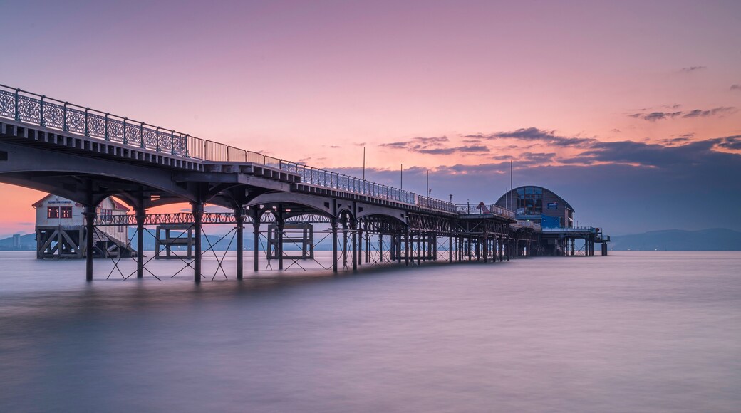 A pier with a lighthouse and a building at the end, extending into calm water.