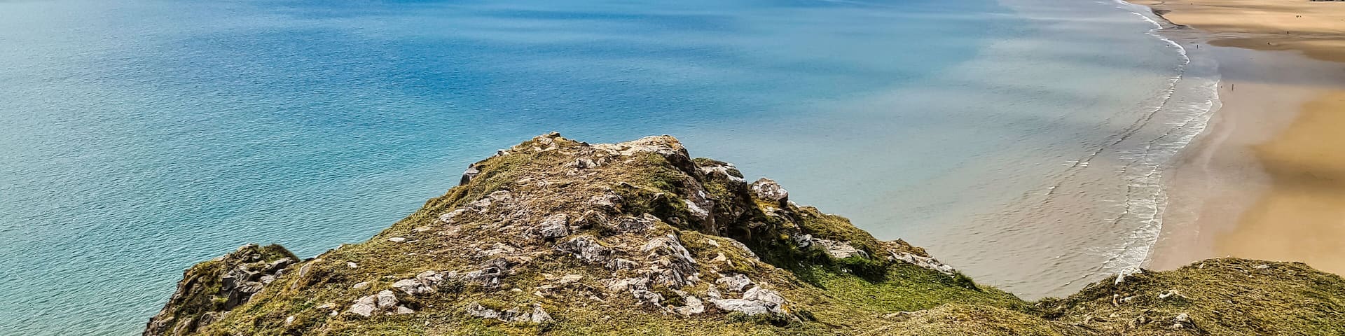 A coastal landscape with a clear blue sea, sandy beach, and rocky cliffs.