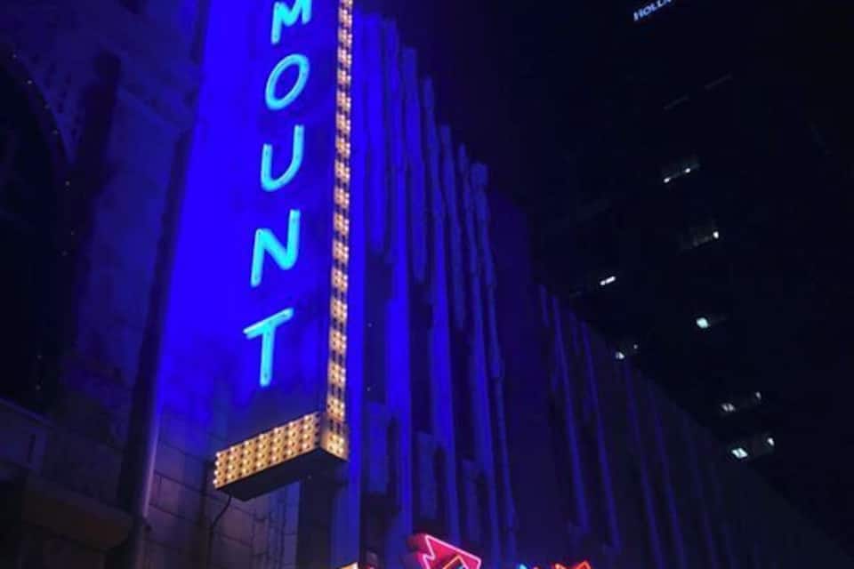 Un letrero de neón del Teatro Paramount con un cartel anunciando fechas de espectáculos.