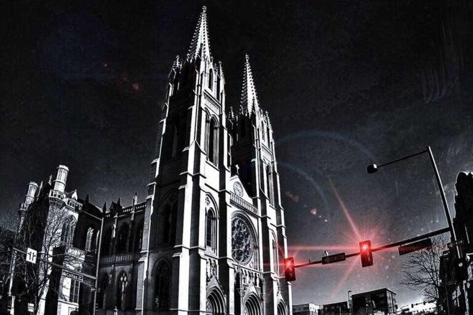 Een gotische kathedraal met twee torens en een grote klokkentoren, tegen een donkere nachthemel.