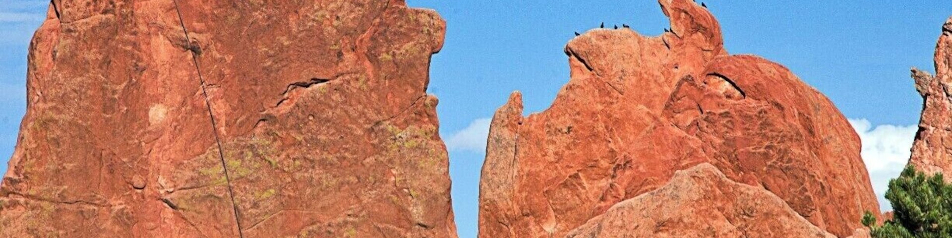 The man on the left has scaled this Mass of rock structure as the birds watch him in the right in the Garden of the Gods, Denver CO, USA. 
Situated right next to Colorado Springs off of US Highway 24 lies a small park aptly named Garden of the Gods. The acreage of the park is rather modest, like Red Rocks, but the sandstone formations are quite striking and memorable. Several massive rocks are decorated with jagged profiles with colors ranging from white, mild orange and rich reds. Spires of up to two pitch height are scattered behind these larger rocks. The park is highly developed and has cement trails in places. Climbing is almost exclusively trad, though there are many routes with drilled angles that don't require gear other than draws. Rock quality varies from formation to formation and can be very crumbly. For Front Range denizens who want to get used to soft desert sandstone, this is a great place to experience it. Get used to an audience, as the crowded park has hundreds of visitors on weekends.