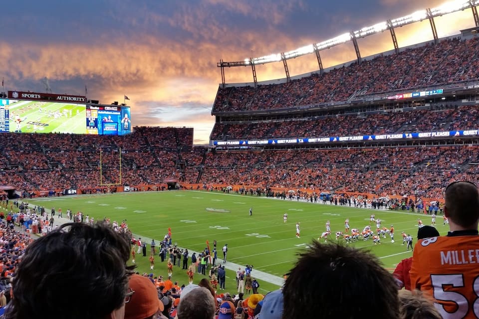A football stadium with a large crowd, a football field, and a scoreboard.