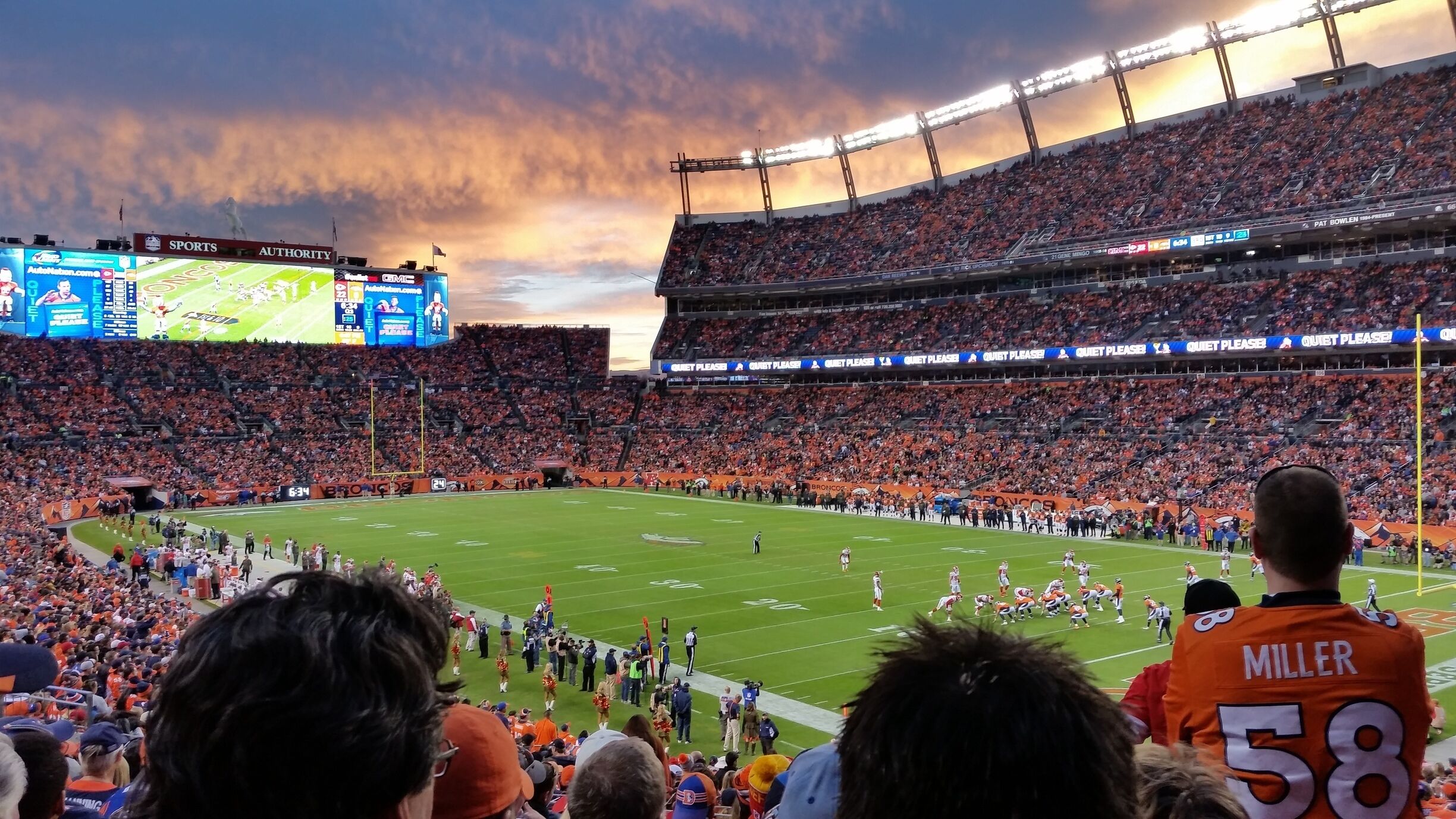 A football stadium with a large crowd, a football field, and a scoreboard.