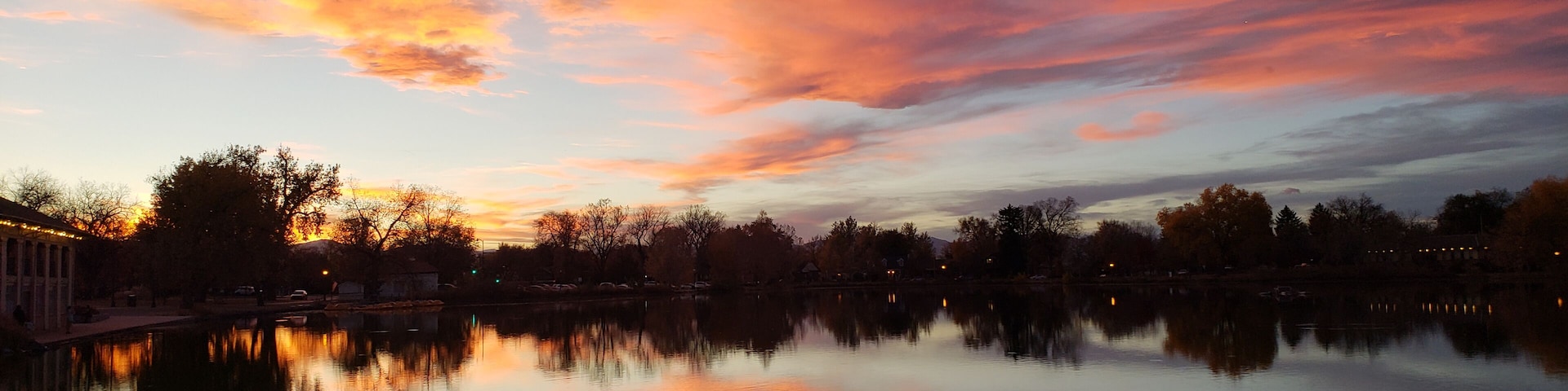 Um pôr do sol sobre um lago calmo, com árvores refletindo as cores do céu.