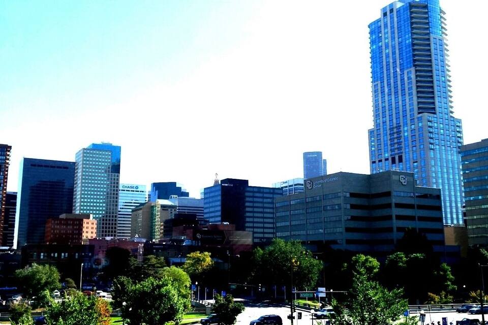 Une vue sur les toits d’une ville, avec de hauts immeubles, dont un gratte-ciel bleu particulièrement imposant.