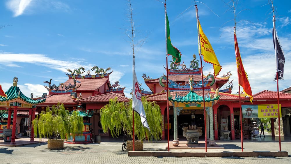 A traditional Chinese temple with colorful flags, a pagoda, and lush greenery.