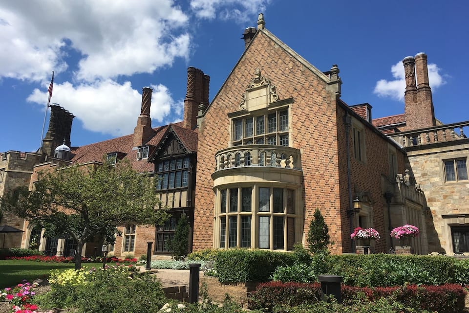 Un bâtiment historique doté d’une tourelle d’angle remarquable, d’une façade en briques et d’un jardin bien entretenu où s’épanouissent des fleurs aux couleurs vives.