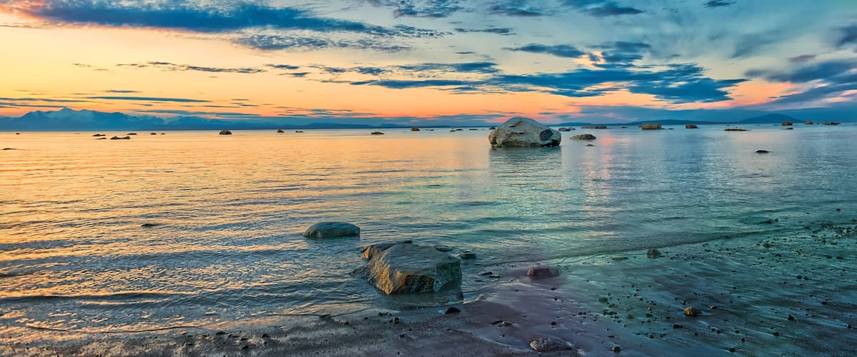 Un paysage côtier avec un coucher de soleil, une aurore boréale verte et des rochers dispersés.
