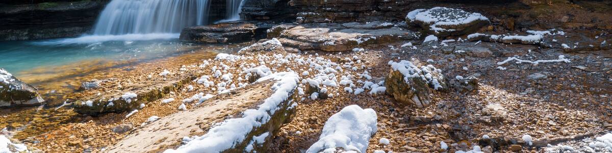 A multi-tiered waterfall cascading over rocky terrain with snow patches.