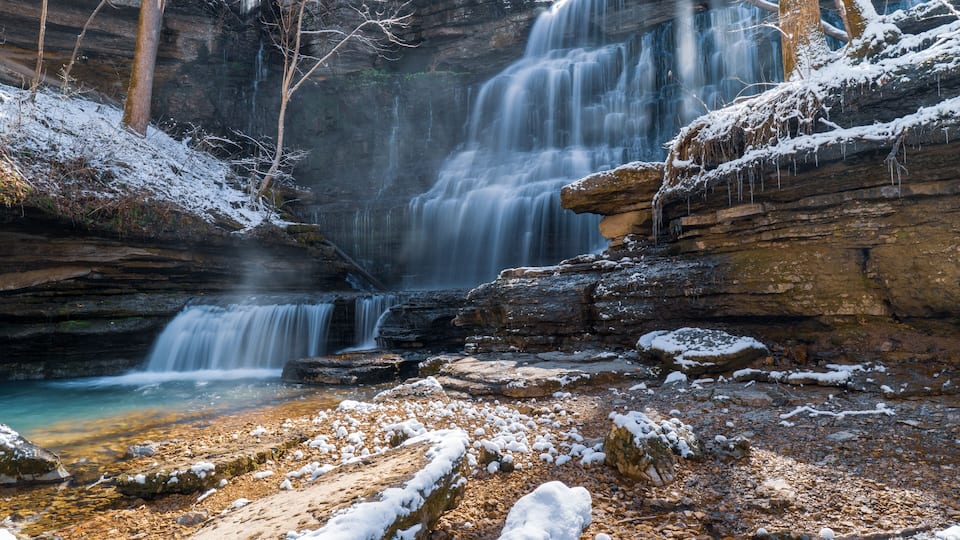 A multi-tiered waterfall cascading over rocky terrain with snow patches.