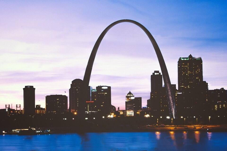 Lo skyline di una città con un ponte ad arco ben visibile, stagliato contro un cielo al crepuscolo.