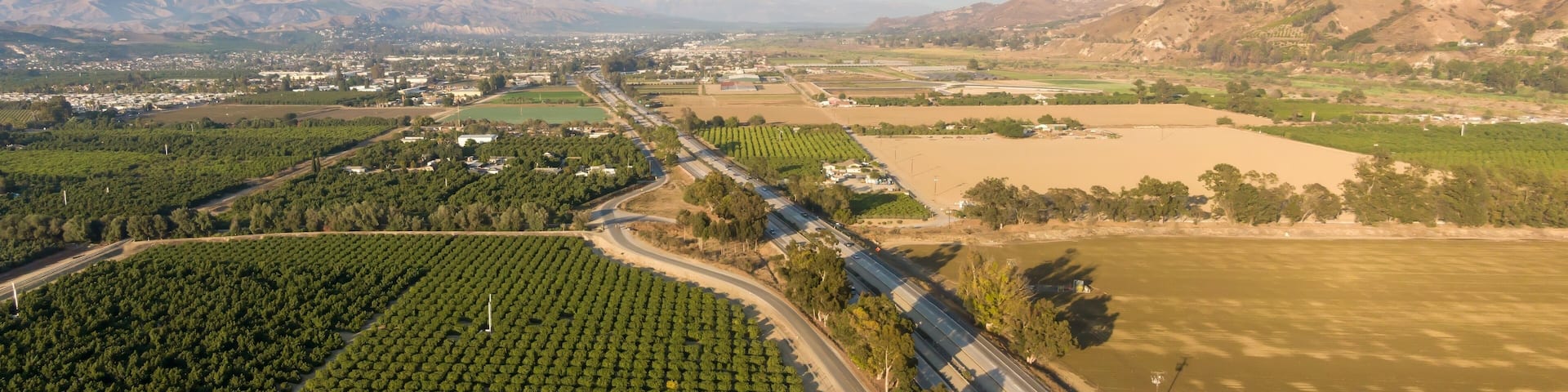 Aerial view of a highway cutting through farmland in Santa Paula, Ventura County, California, USA. Cars and trucks travel along the road, connecting rural areas.
