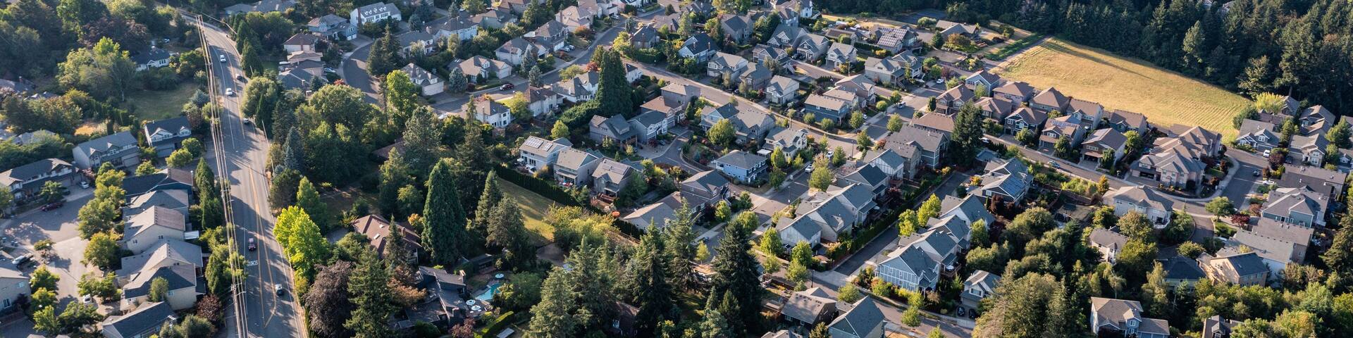 Aerial drone view of Tigard, Oregon, showcasing suburban neighborhoods, tree-lined streets, commercial areas, parks, and roads, with a mix of residential and business districts in the Portland metro