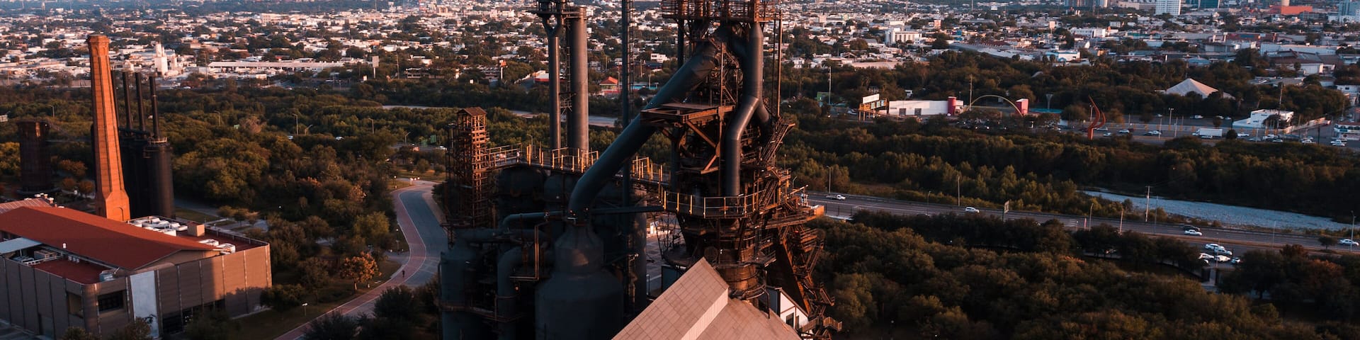 A large industrial complex with multiple tall chimneys, surrounded by a cityscape and a mountain in the background.