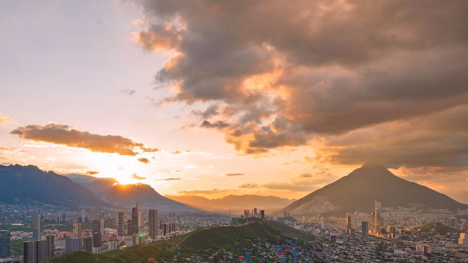 A cityscape with a prominent mountain in the background, a clear sky, and a sunset.