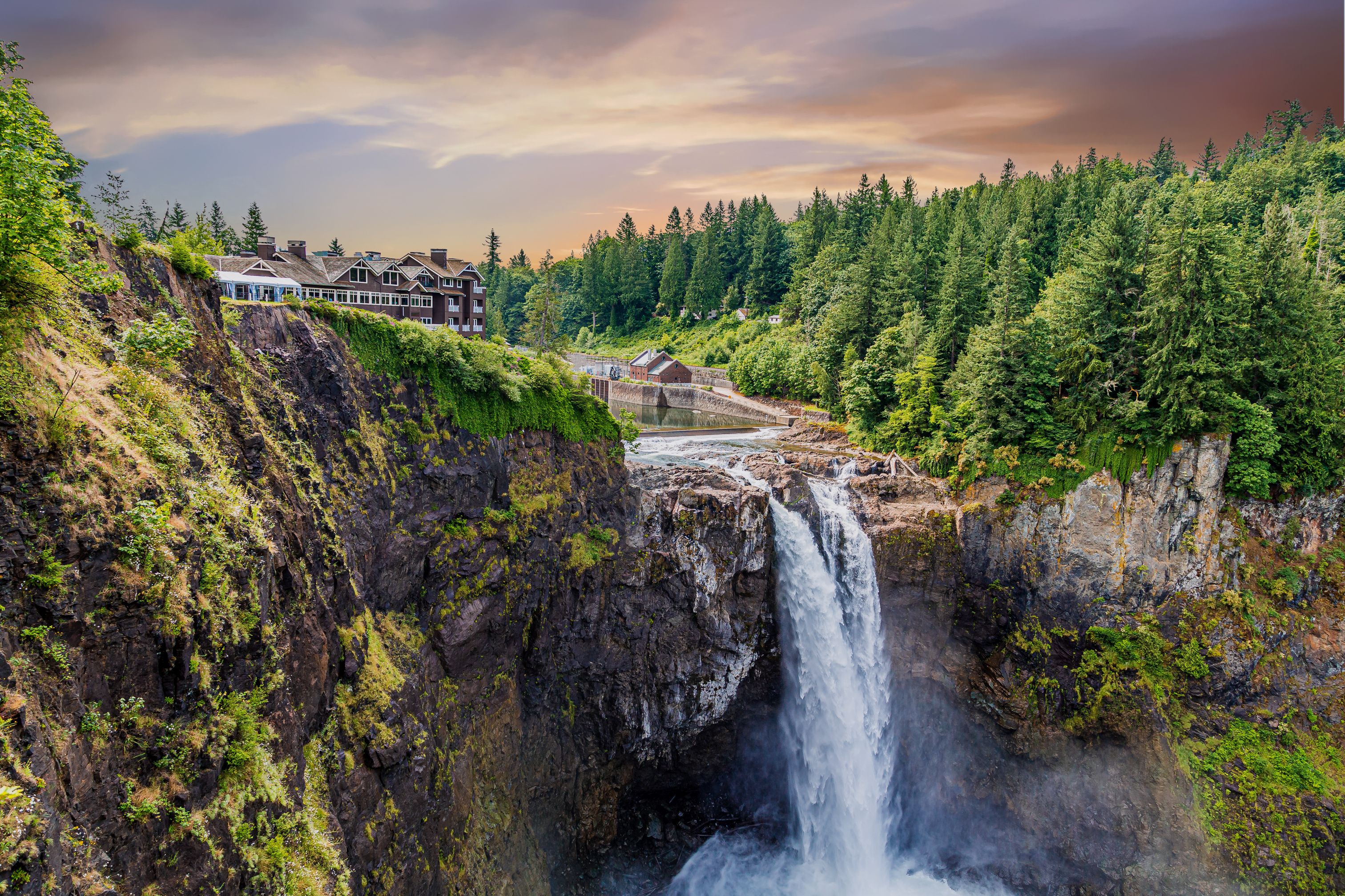 A waterfall cascading down a rocky cliff surrounded by lush greenery and residential buildings.