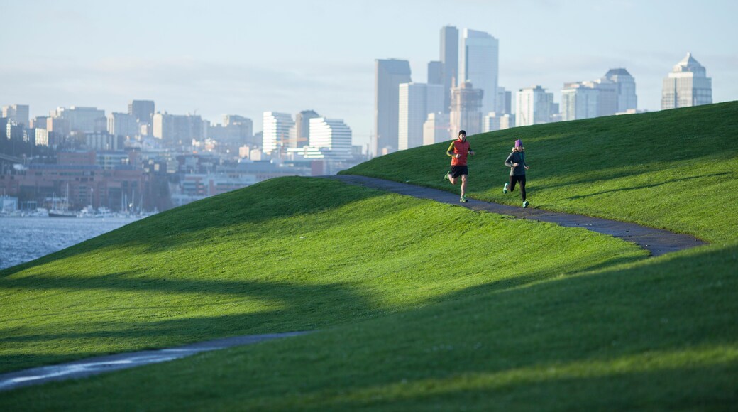An adult man and woman running the paved path through Gasworks Park with the Seattle cityscape in the background. Washington State.