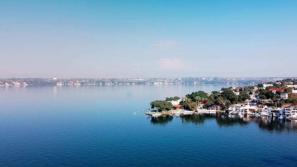A calm lake with a small island featuring buildings and trees.
