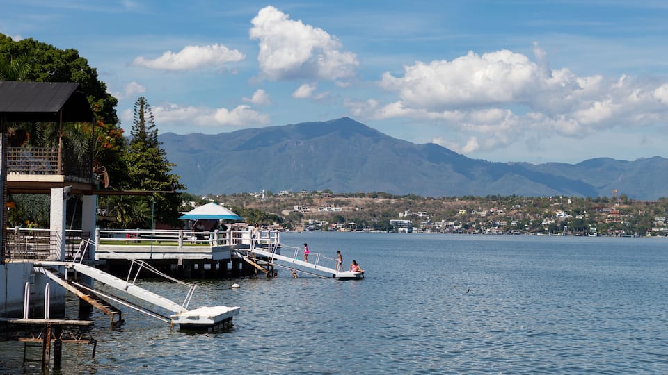A lake with a dock, a small boat, and mountains in the background.