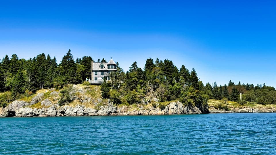 A coastal house surrounded by dense forest and rocky shoreline.