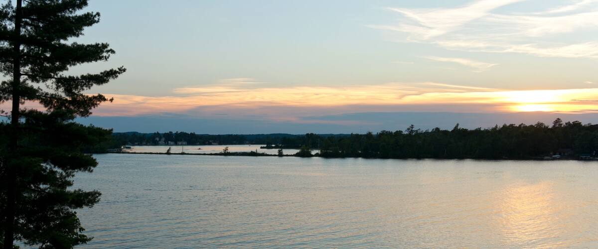 A sunset over a calm lake with a dock and people standing on it.