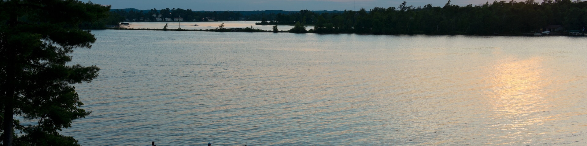 A sunset over a calm lake with a dock and people standing on it.