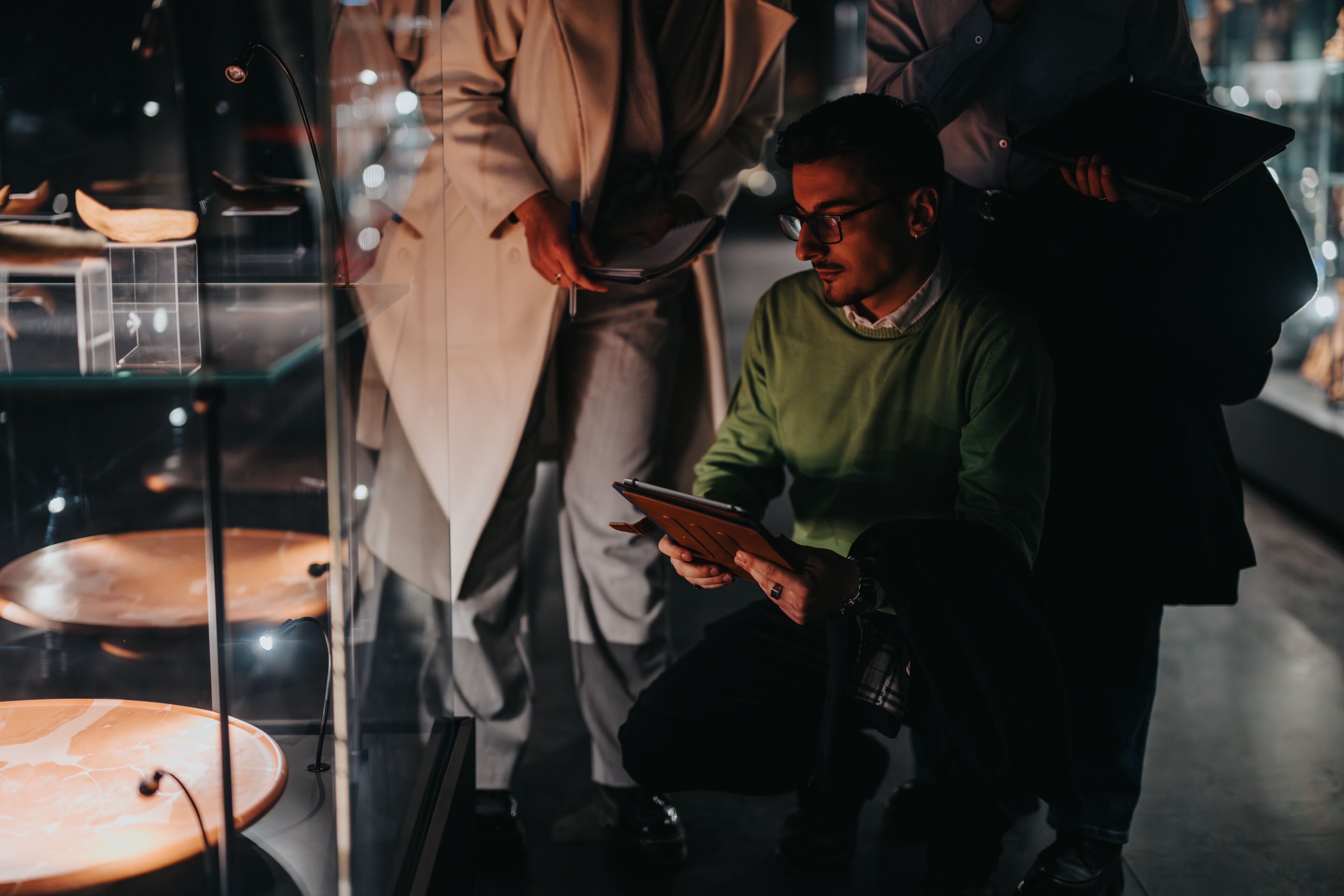 Group of people exploring exhibits in a dimly lit museum environment, showcasing cultural artifacts and fostering curiosity, contemplation, and collaboration in an educational and artistic setting.
