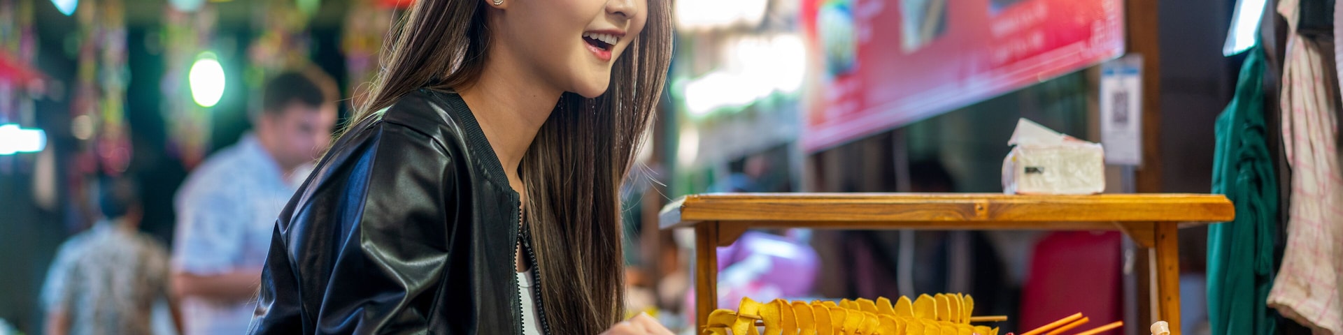 Asian woman enjoying street food at Chiang Mai Walking Street Night Bazaar. Young traveler exploring vibrant night market in Thailand.
