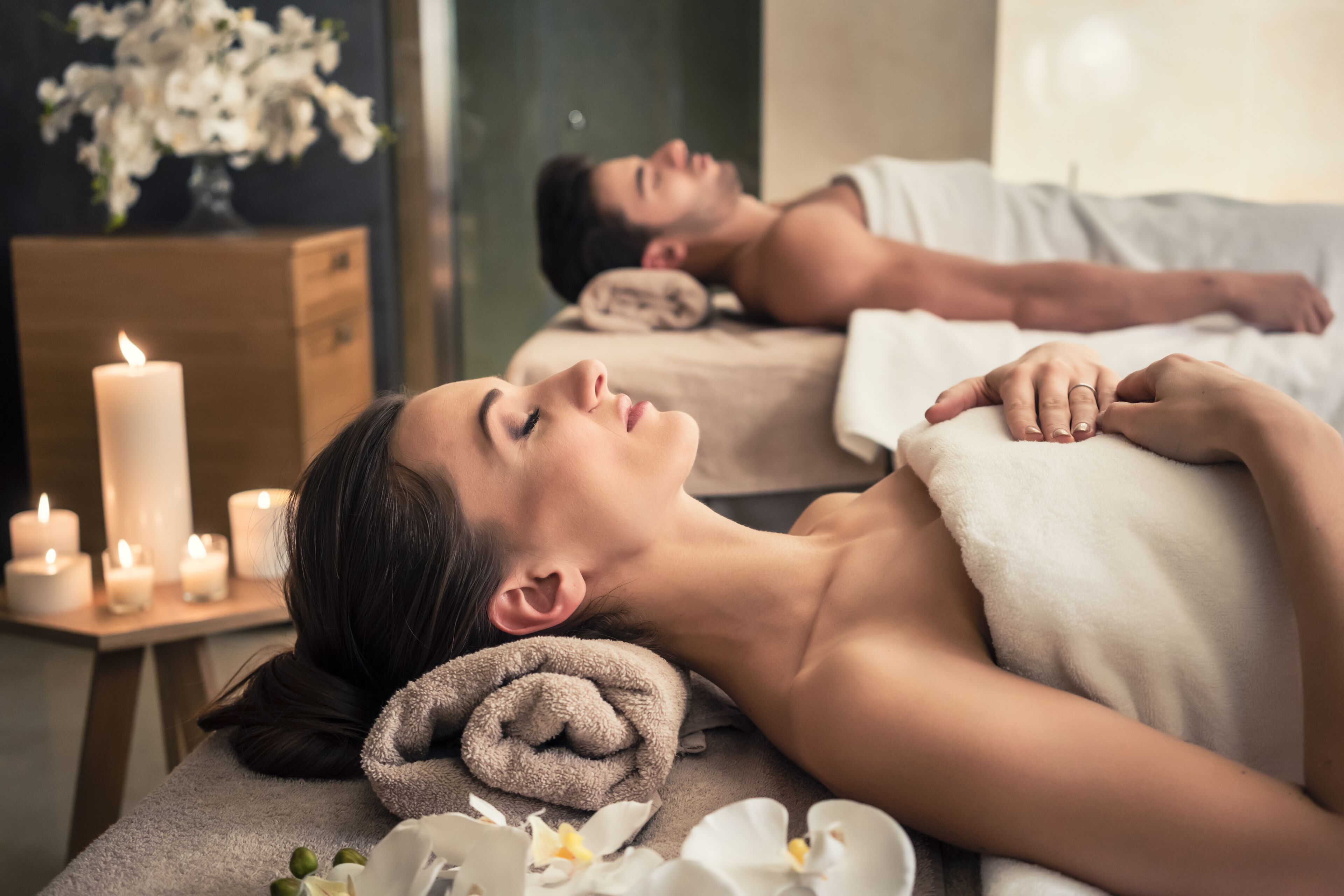 Um quarto de spa com duas pessoas recebendo massagem, um armário de madeira e velas acesas.